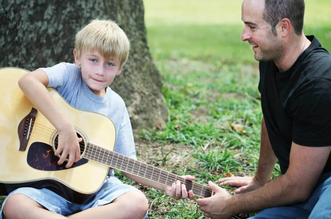 young boy learning to play guitar with help from his Big Brother