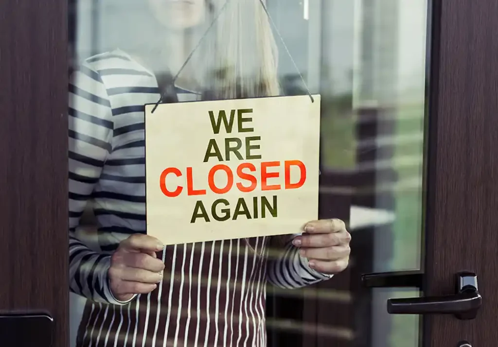 Woman standing behind closed again sign in shop window