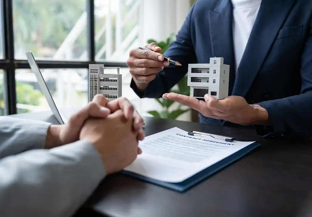 close up of two people meeting in an office next to model of a condo development. Only hands and arms visible.