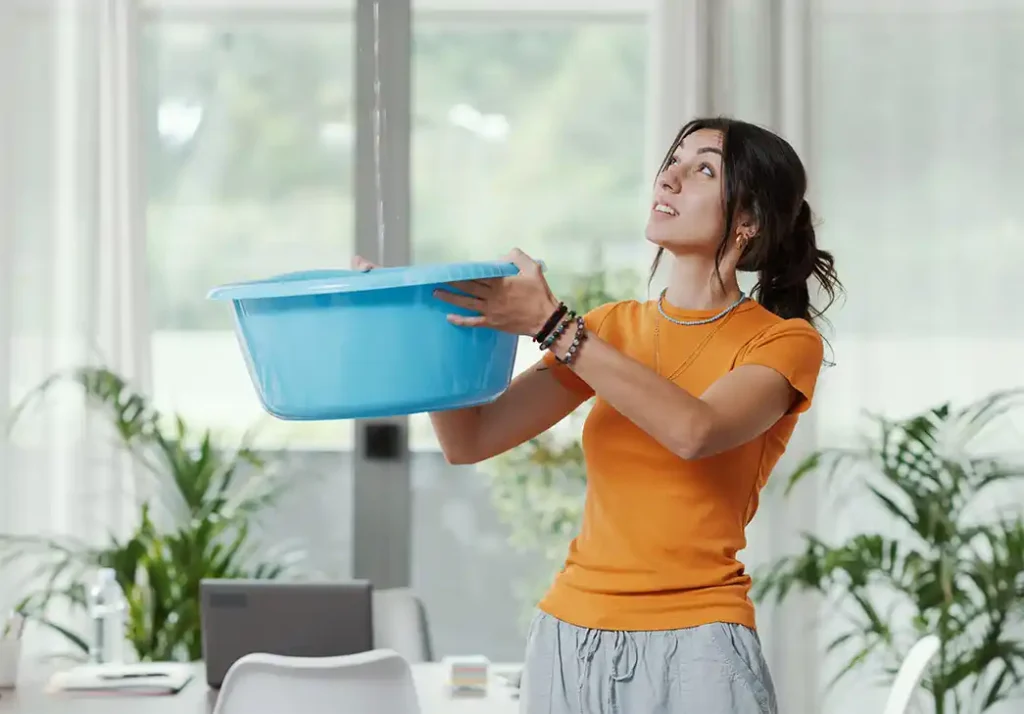 Young woman holding up a basin to catch dripping water from her ceiling