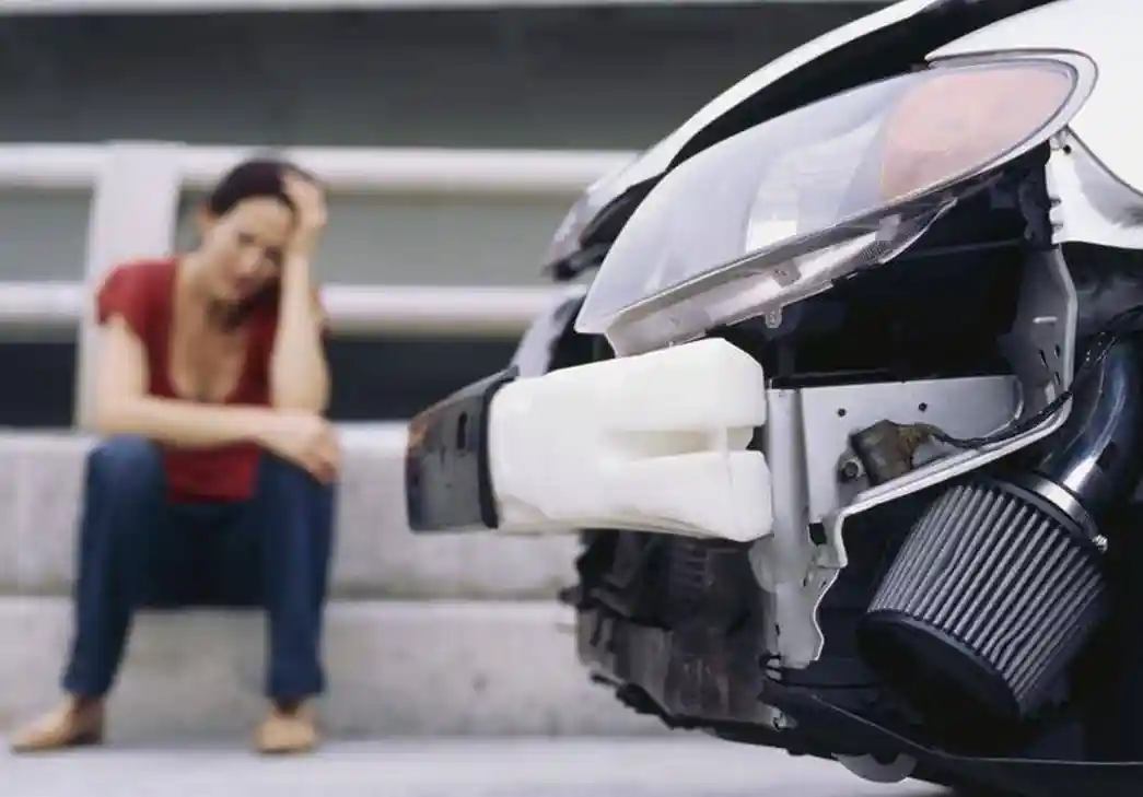young woman sitting on a curb in front of damaged car