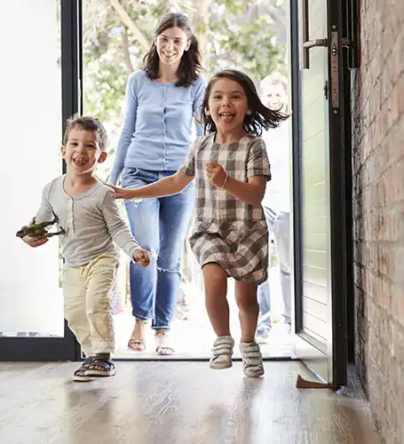 Two kids running into the house with mom in the background