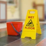 Wet floor sign next to red bucket on a tiled floor