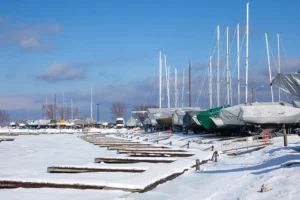 Sailboats line the perimeter of a marina during the winter months when the harbor is frozen. The boats are winterized and covered up.