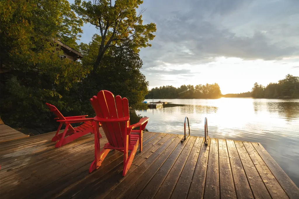 Two red Muskoka chairs sit facing the sunrise on a dock